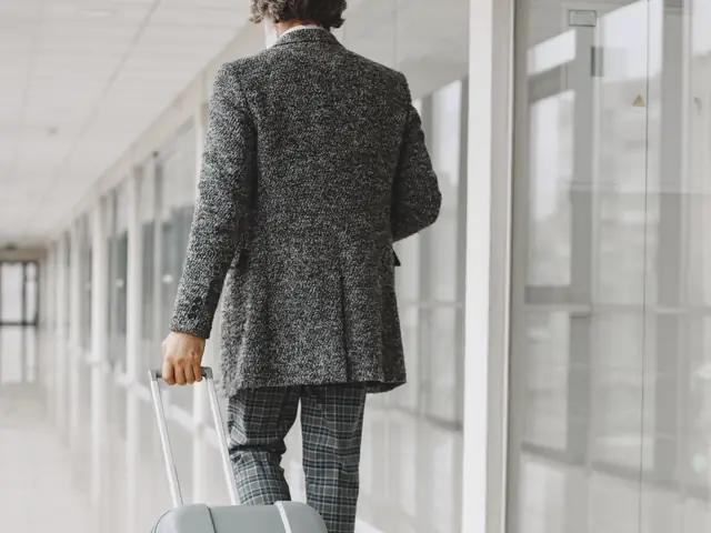 Homem de terno, de costas, puxando a mala no corredor de um aeroporto