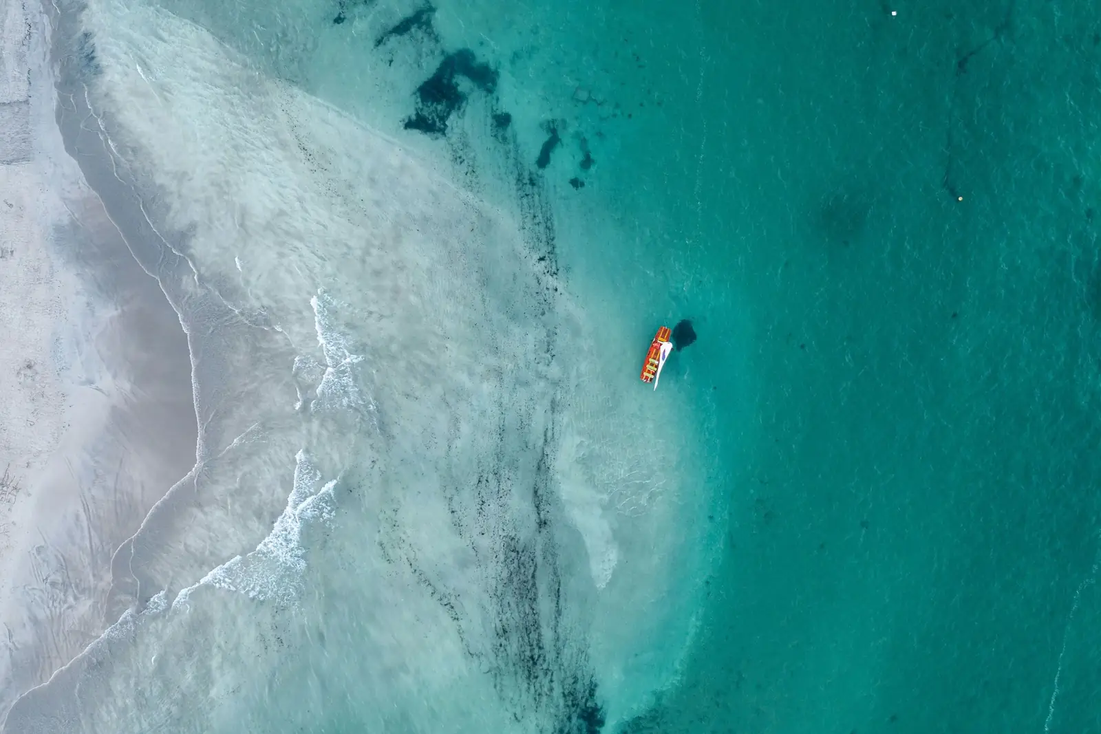 Mar verde-azulado visto do alto, com um barquinho perto da faixa de areia
